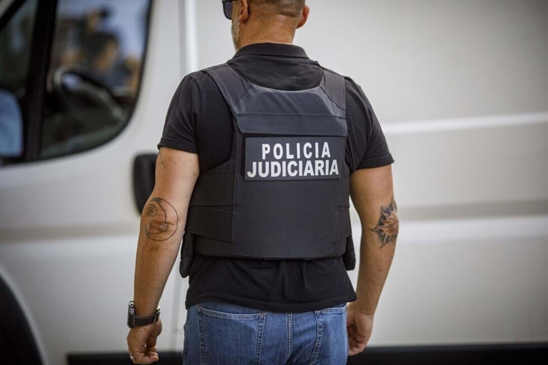 Agente da Polícia Judiciária de costas com colete identificativo