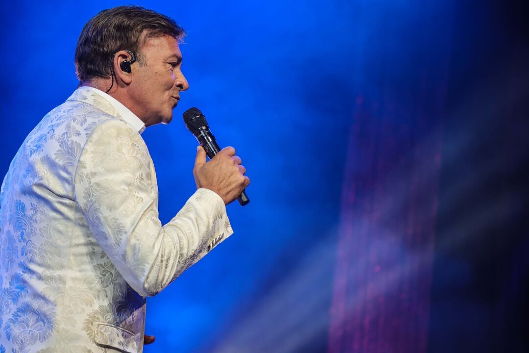 Artista atua com um microfone num palco com luzes azuis