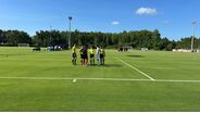 Árbitros e jogadores de futebol reunidos num campo relvado sob céu azul