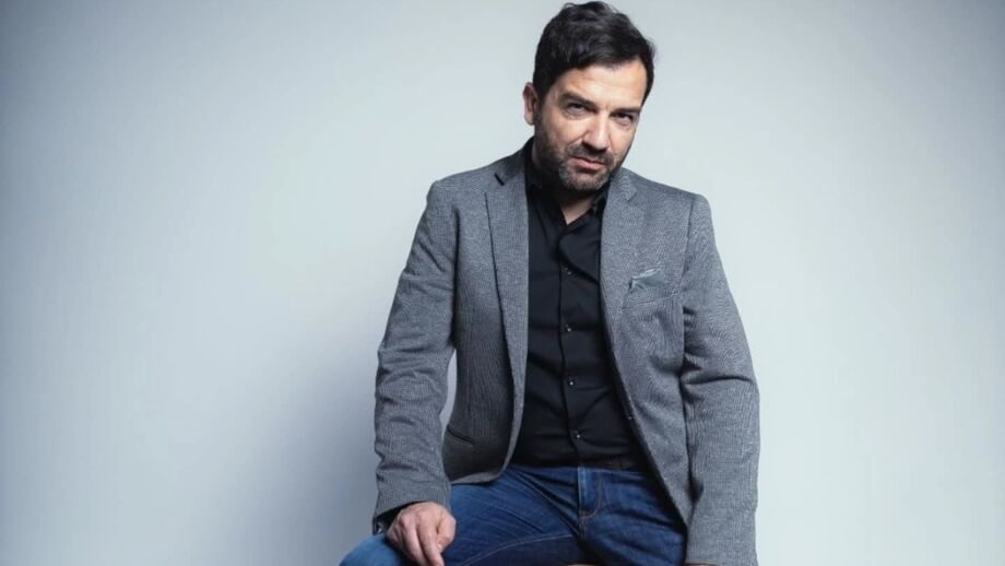 Homem posa com blazer cinza e camisa preta
