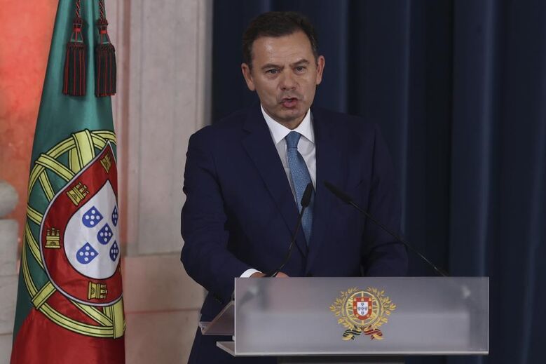 Figura pública discursa ao lado da bandeira de Portugal