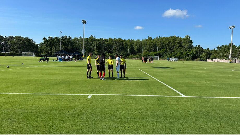 Árbitros e jogadores de futebol reunidos num campo relvado sob céu azul