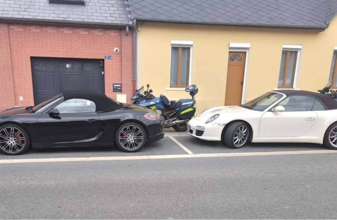 Dois carros e uma mota estacionados numa rua perto de edifícios