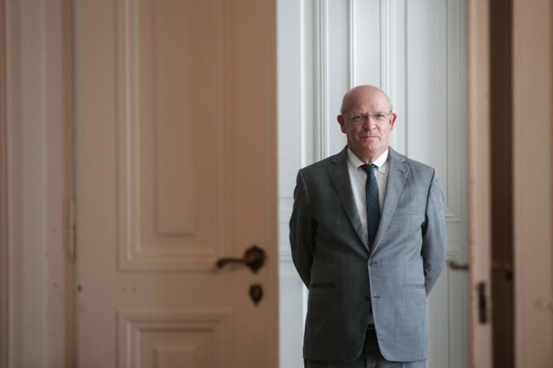 Um homem de óculos e fato posa em frente a uma porta