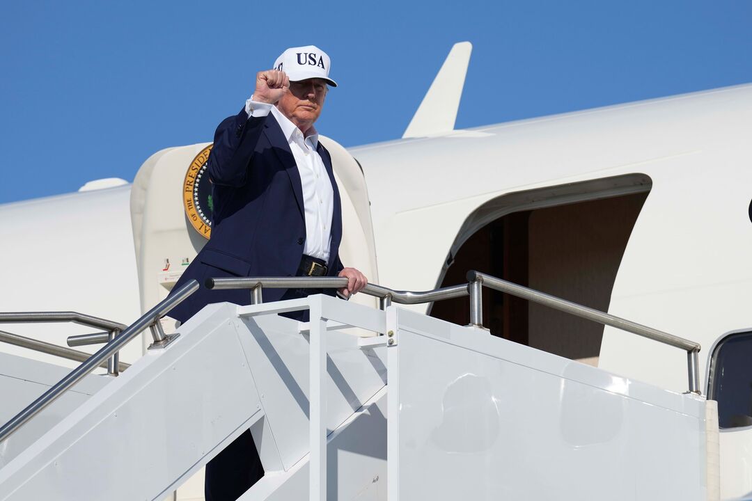 Donald Trump desce as escadas de um avião com boné dos EUA