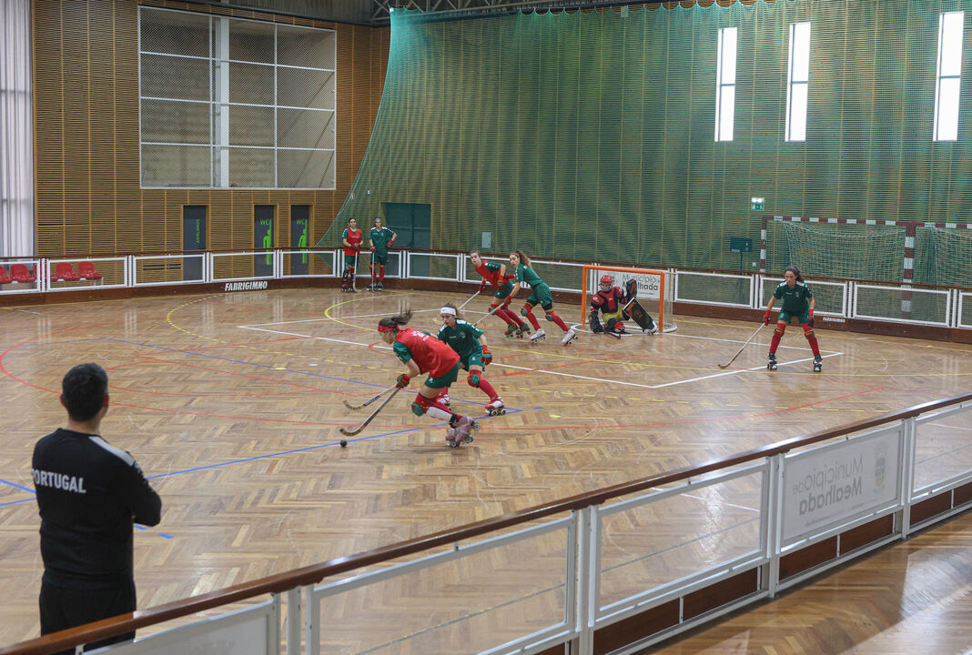 Jogo de hóquei em patins com atletas em campo e um treinador de Portugal a assistir