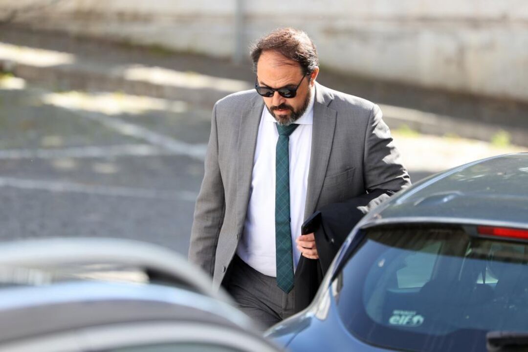 Homem de óculos de sol, fato e gravata perto de carros