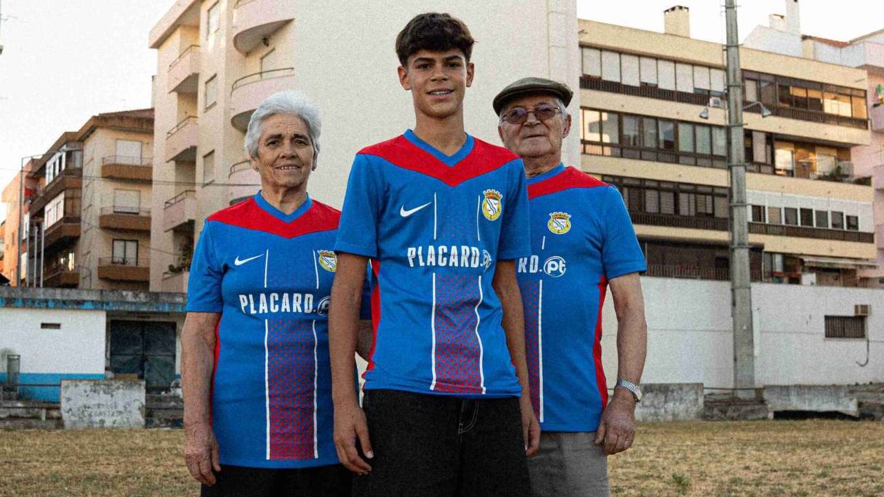 Avó, neto e avô vestem camisolas de futebol num campo relvado