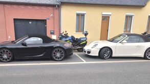 Dois carros e uma mota estacionados numa rua perto de edifícios