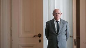 Um homem de óculos e fato posa em frente a uma porta