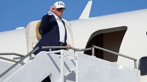 Donald Trump desce as escadas de um avião com boné dos EUA