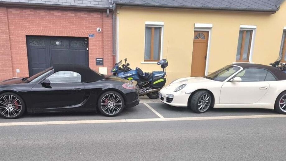 Dois carros e uma mota estacionados numa rua perto de edifícios