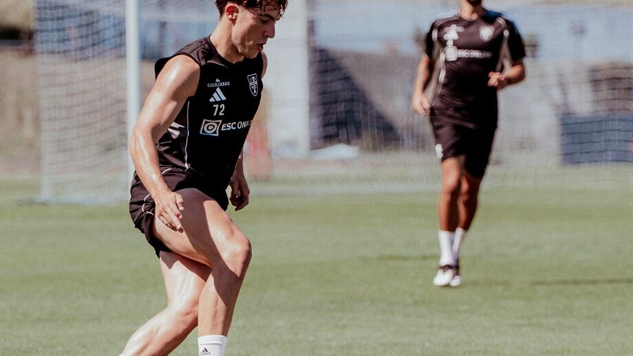 Jogador de futebol treina com bola em campo relvado