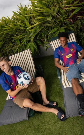 Dois homens sorriem com camisolas do Barcelona e calções de banho, um segura uma bola