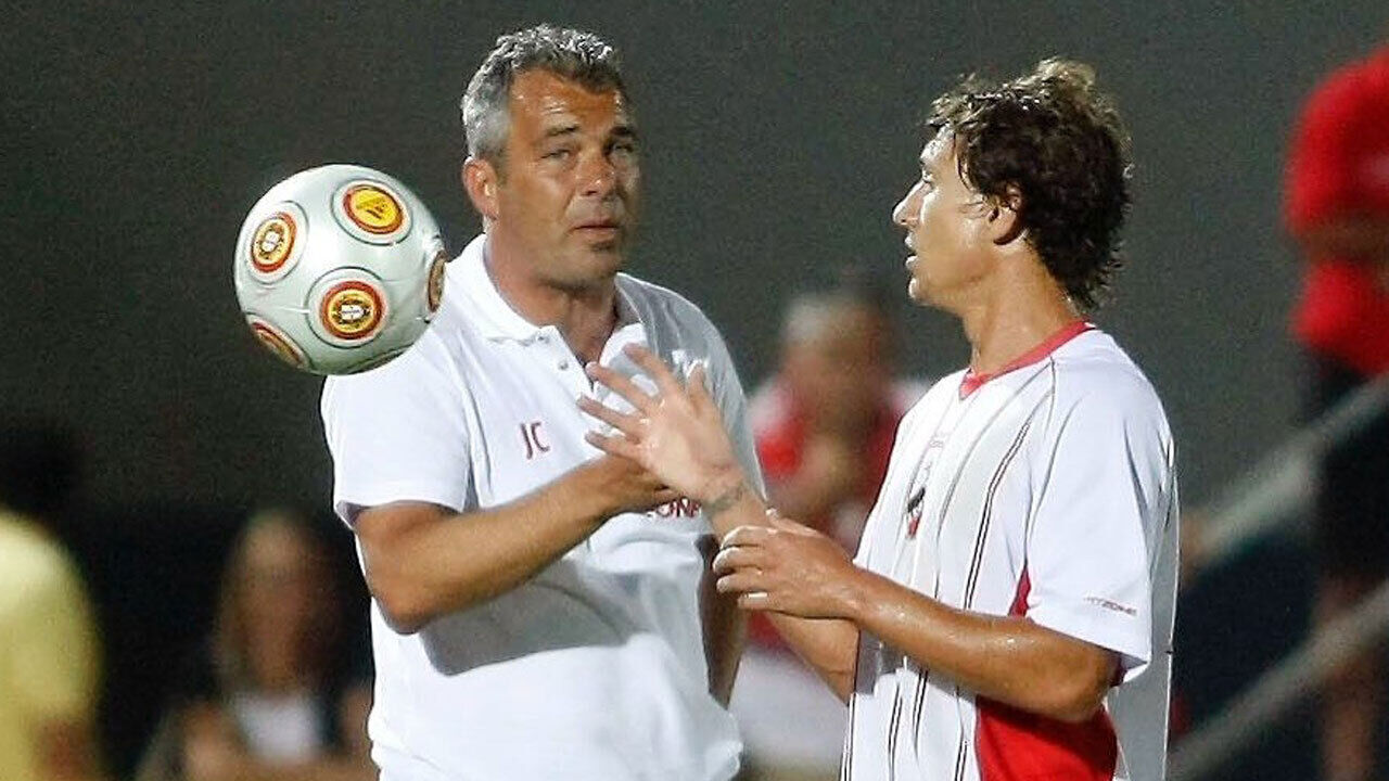 Treinador e jogador de futebol conversam com uma bola perto