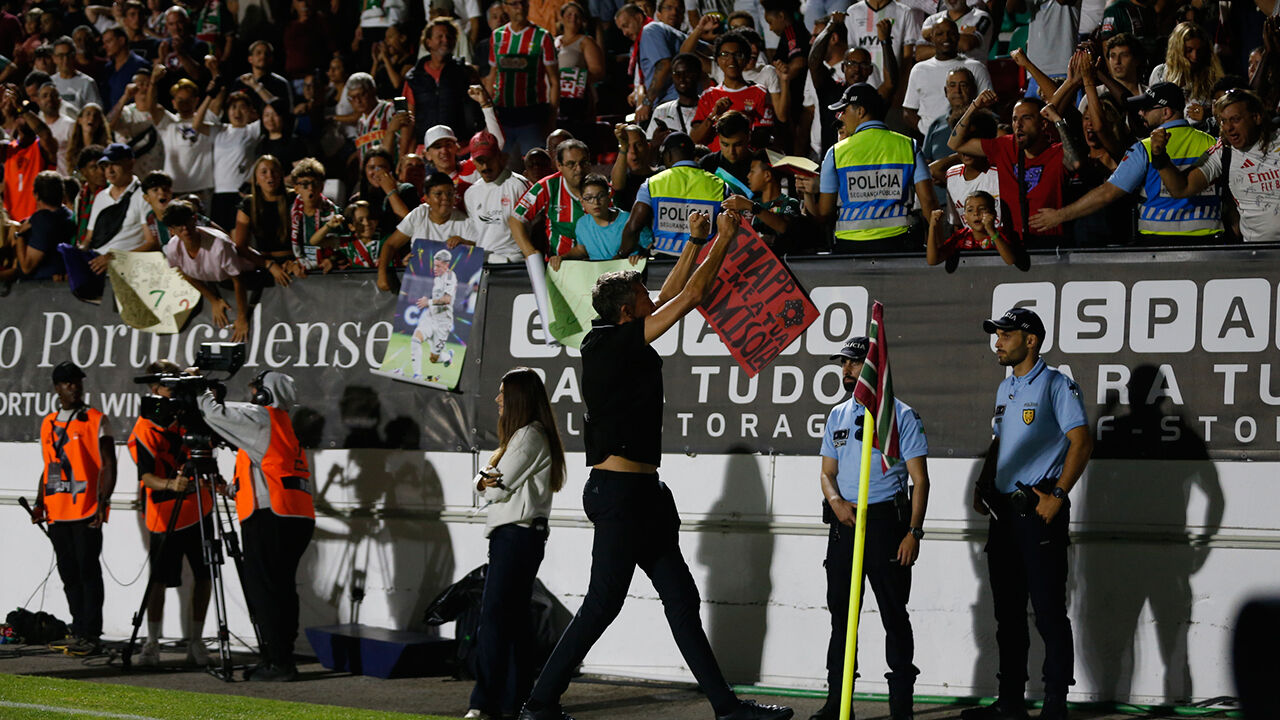 Fãs e polícias num jogo de futebol; um adepto segura um cartaz