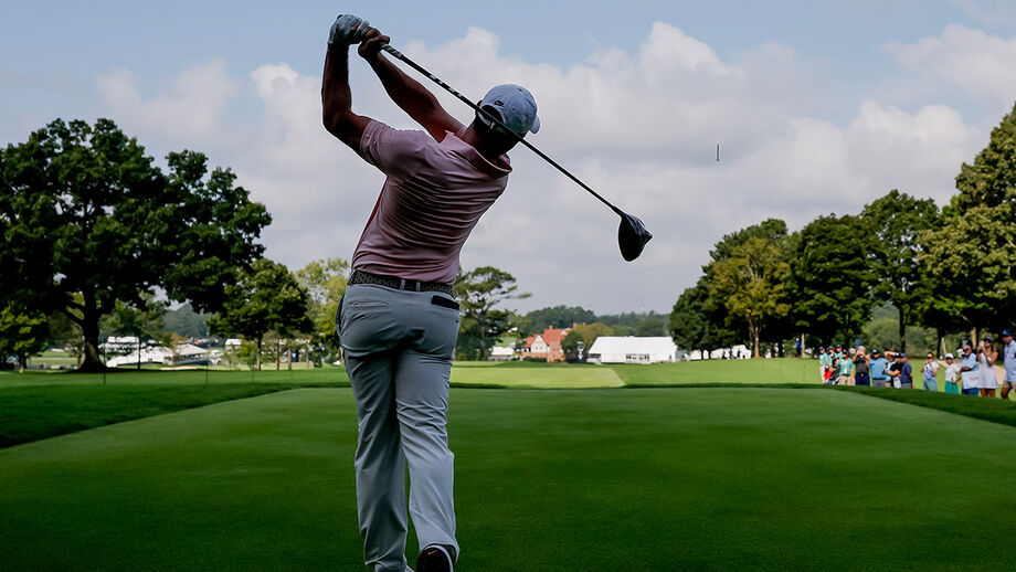 Golfista executa swing num campo verdejante.
