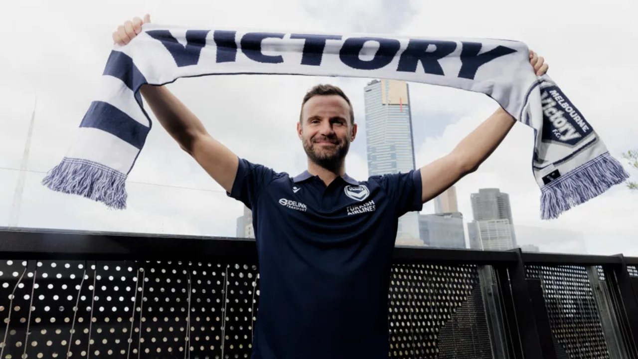 Homem exibe cachecol do Melbourne Victory com o horizonte da cidade