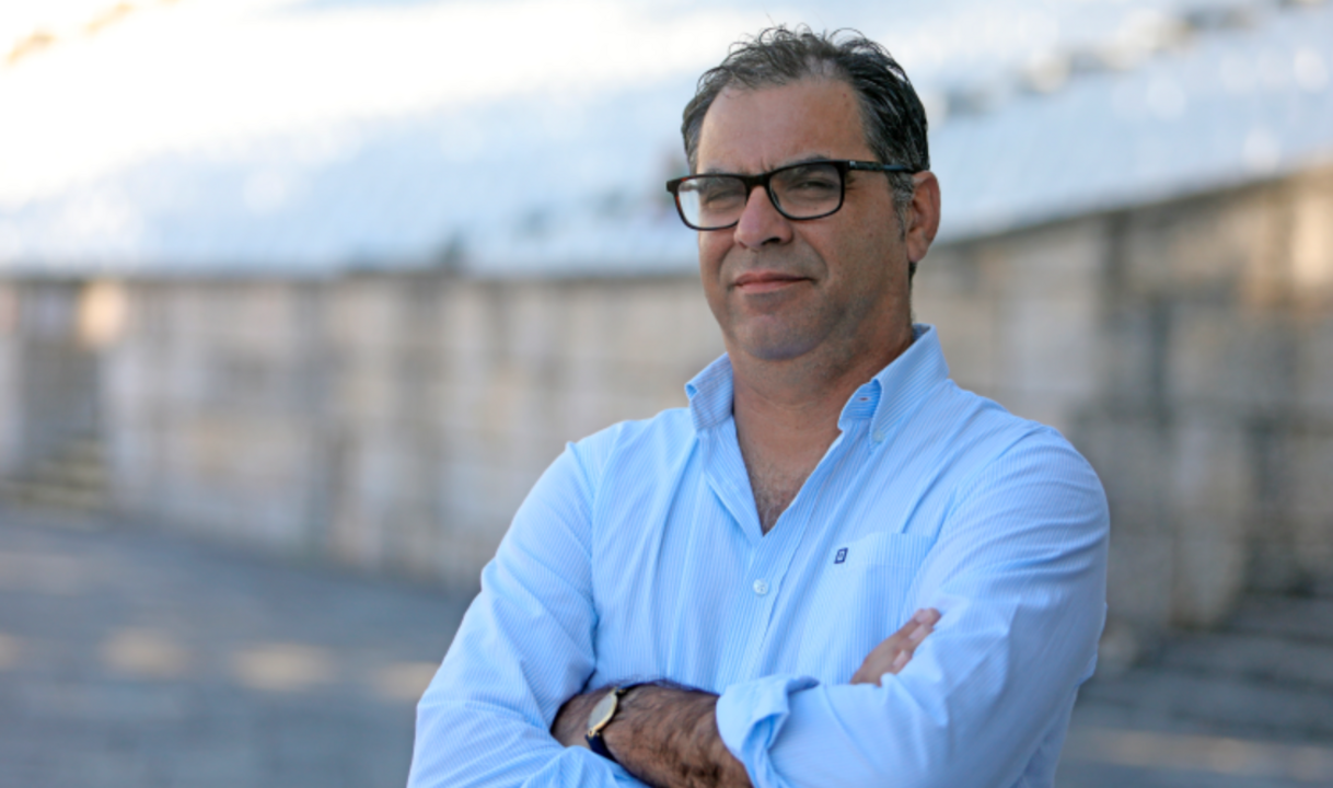 Homem de óculos e camisa azul pousa para a fotografia com os braços cruzados