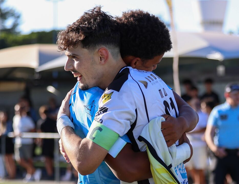 Dois jogadores de futebol abraçam-se no campo