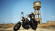 Homem com t-shirt "Sarony Lisboa" posa com mota, junto a torre de água