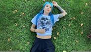 Mulher com cabelo azul e tatuagens relaxa na relva