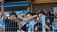 Jovens adeptos apoiam equipa no estádio, com cachecóis e camisolas
