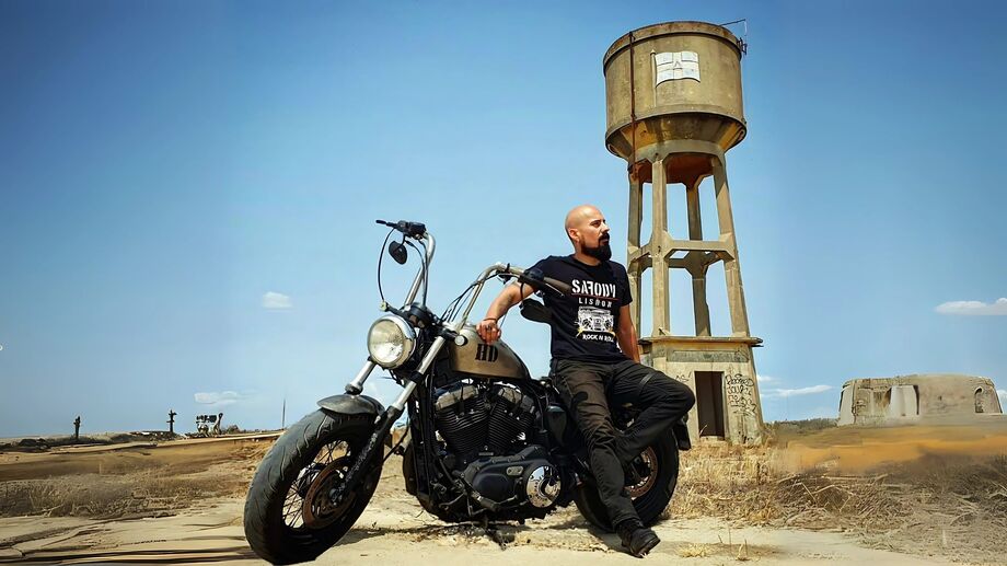 Homem com t-shirt 'Sarony Lisboa' posa com mota, junto a torre de água