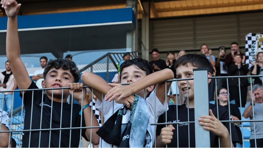 Jovens adeptos apoiam equipa no estádio, com cachecóis e camisolas