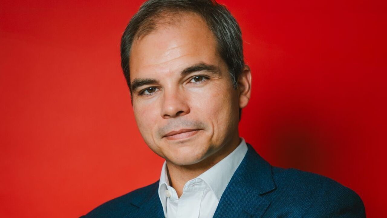 Homem de fato azul, camisa branca e relógio posa com braços cruzados