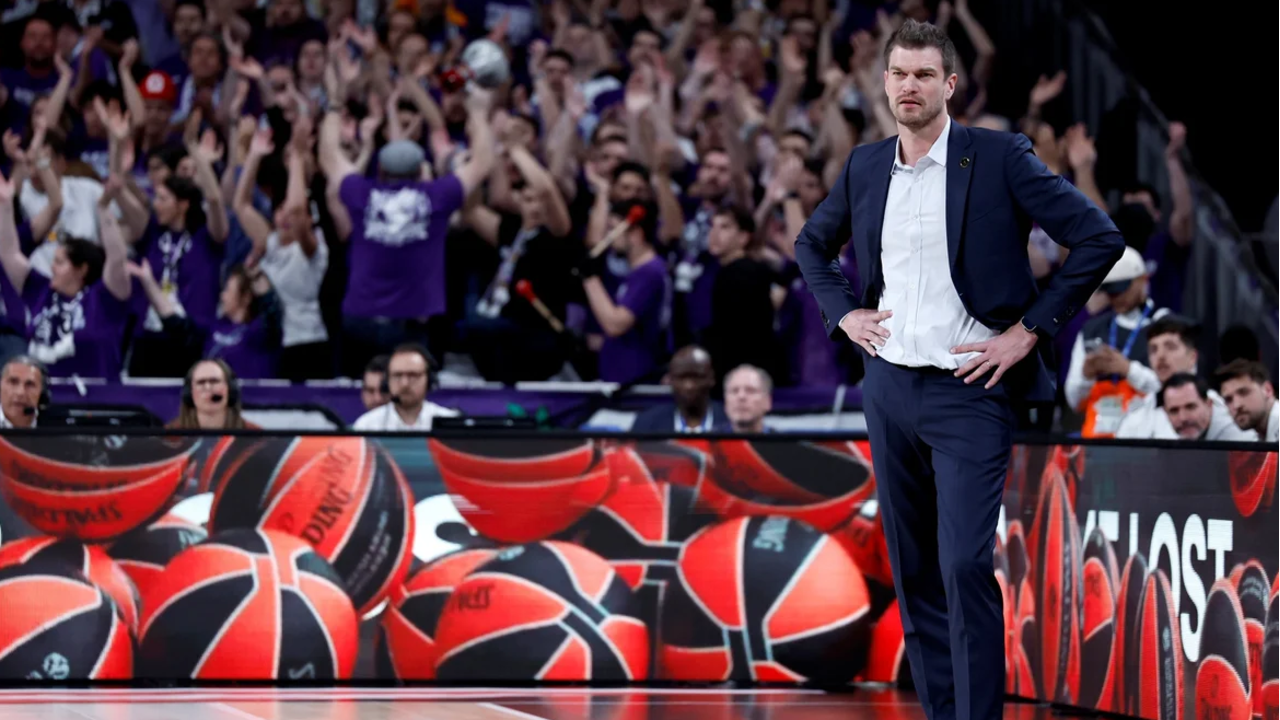Treinador de basquetebol observa jogo com público animado ao fundo
