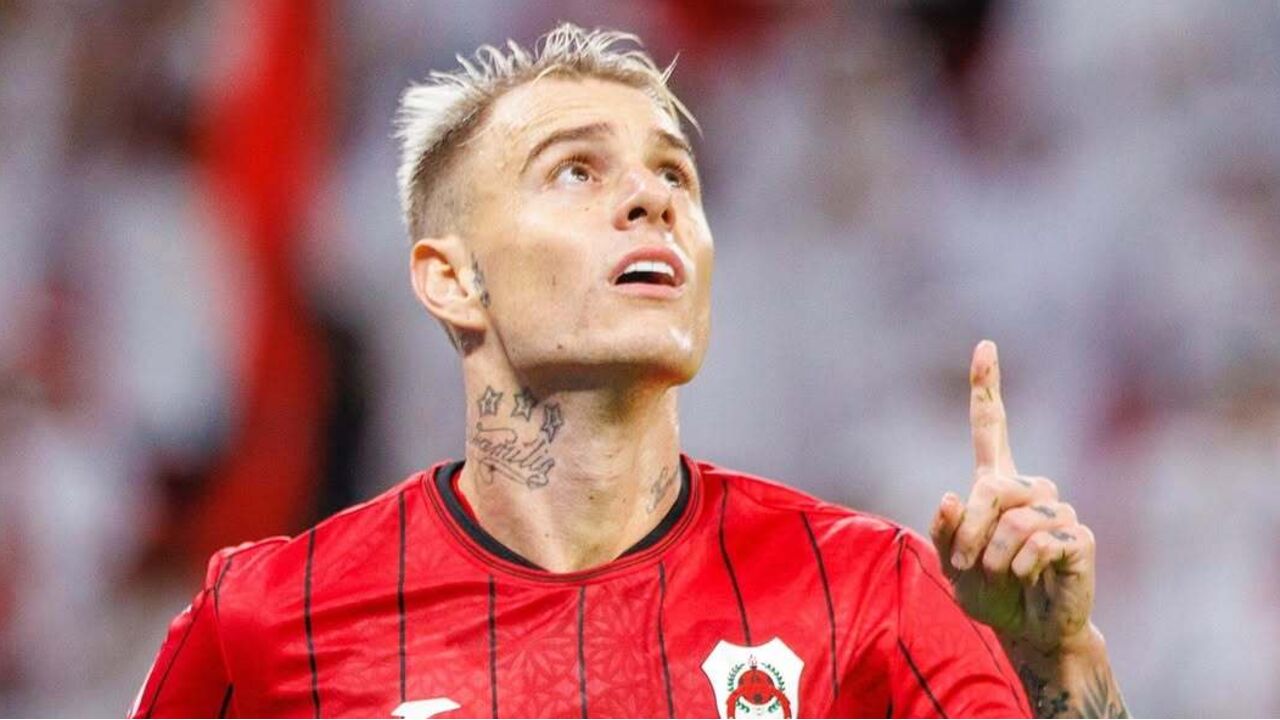 Jogador de futebol com camisola vermelha aponta para cima