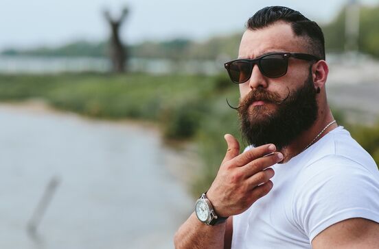 Homem de barba usa óculos de sol e relógio; kit Cusmay é o segredo para barba impecável
