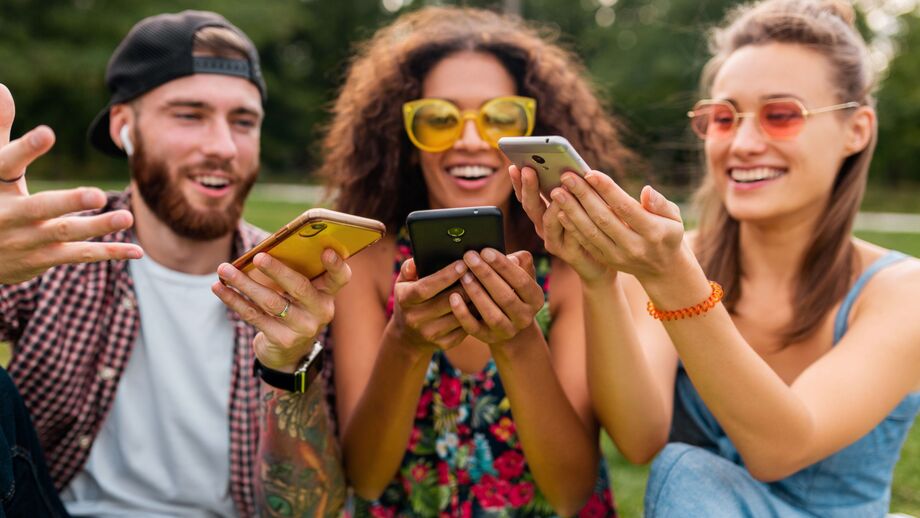 Grupo de amigos sorridentes usa smartphones no parque