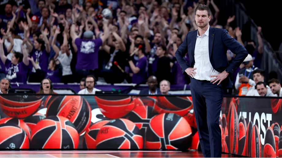 Treinador de basquetebol observa jogo com público animado ao fundo