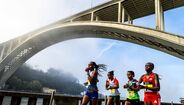 Atletas correm na Maratona do Porto sob a Ponte da Arrábida.
