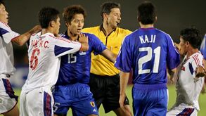 Jogo de futebol tenso entre Coreia do Norte e Japão com árbitro a intervir