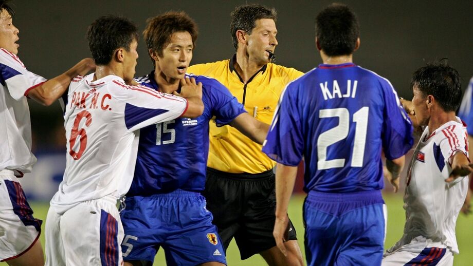Jogo de futebol tenso entre Coreia do Norte e Japão com árbitro a intervir