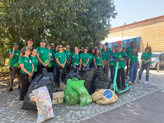 Grupo de pessoas participa numa ação de limpeza ao ar livre com sacos cheios de lixo
