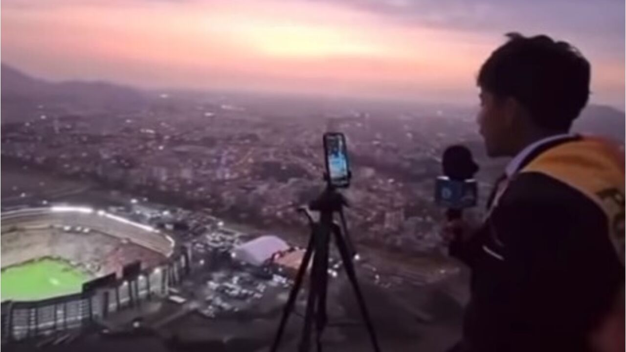 Jornalista filma estádio e cidade ao pôr do sol, com telemóvel e microfone