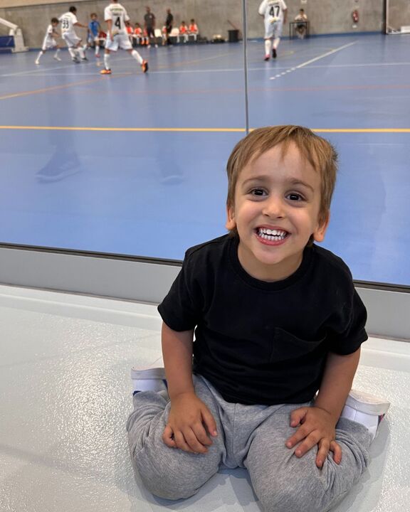 Dinis sorri enquanto assiste a um jogo de futsal, com apoio da Associação Salvador.
