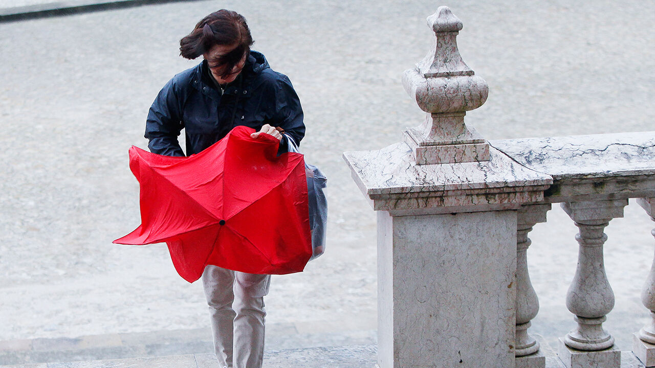 Chuva e vento afetam a mulher com guarda-chuva vermelho