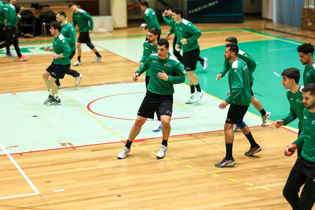 Jogadores de andebol treinam num campo com equipamento verde e preto