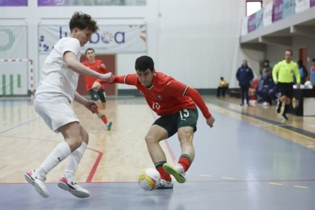 Jogo de futsal com atletas em ação e um árbitro a observar a partida
