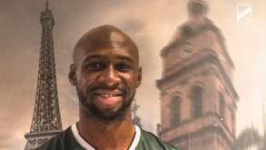 Homem sorri junto à Torre Eiffel e uma torre ao fundo