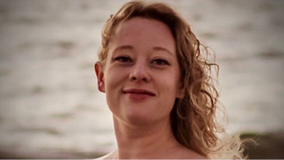 Mulher sorri com vestido vermelho em frente ao mar