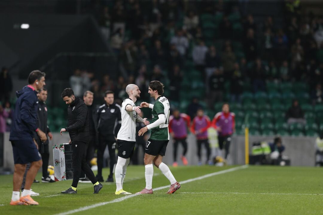 Futebolistas cumprimentam-se em campo, perante a assistência nas bancadas
