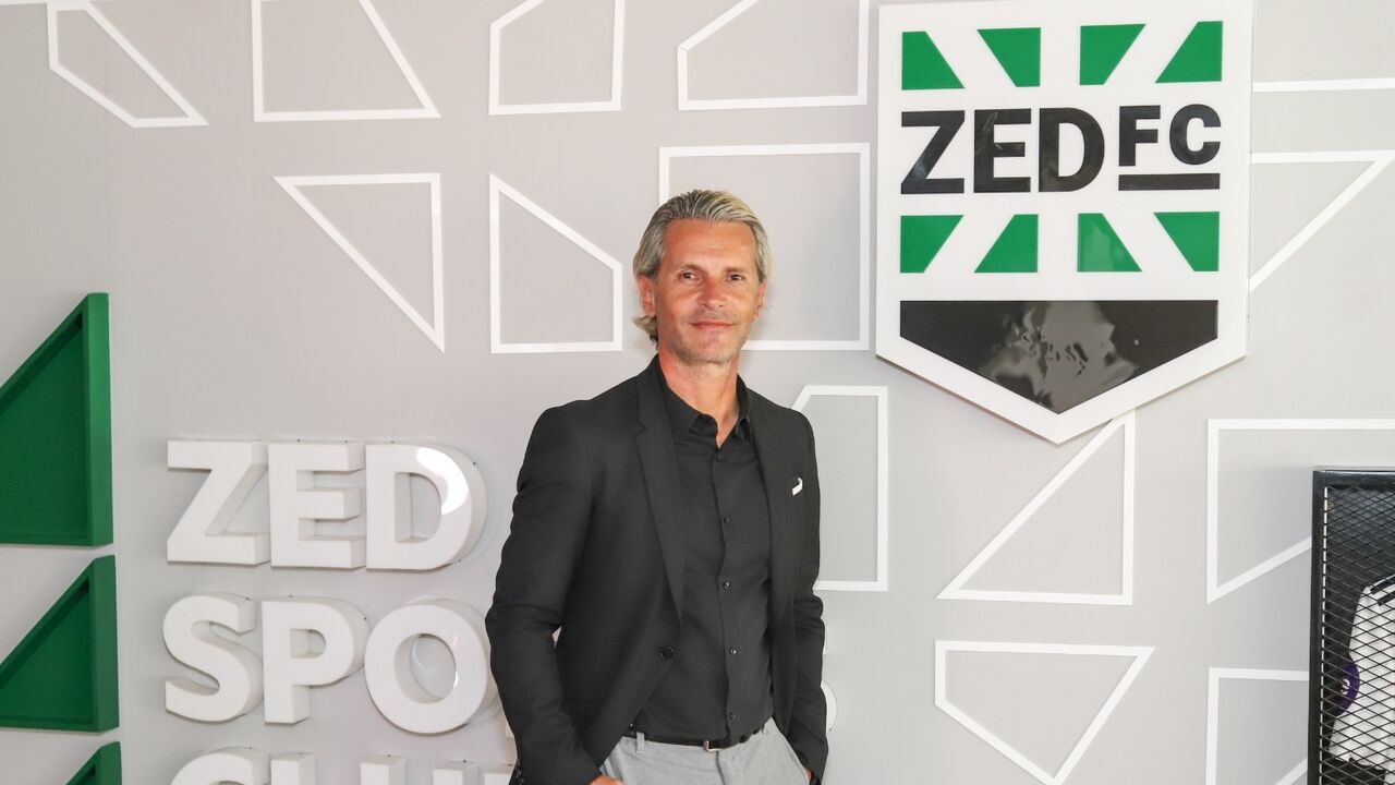 Um homem posa junto ao logótipo do ZED FC