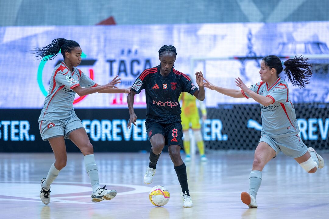Jogadora do Benfica tenta passar pelas adversárias durante jogo de futsal