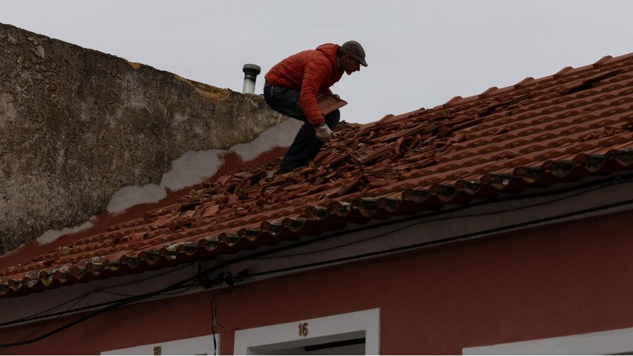 Homem repara telhado danificado pela tempestade Kristin em Portugal